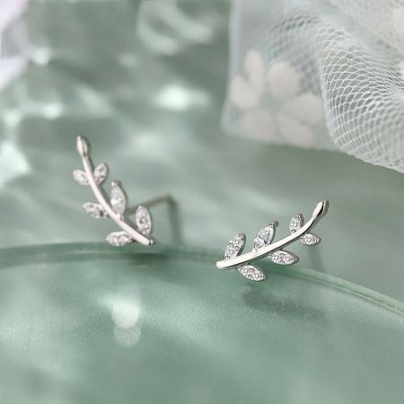 925 Zilver CZ Zirkon Olijfbladeren Stud Oorbellen - Een paar 925 sterling zilveren olijfblad stud oorbellen met sprankelende CZ zirkon stenen, elegant weergegeven op een groene satijnen achtergrond.