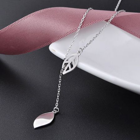 El collar Y-chain con borlas de hoja exhibido en un soporte profesional de joyería.