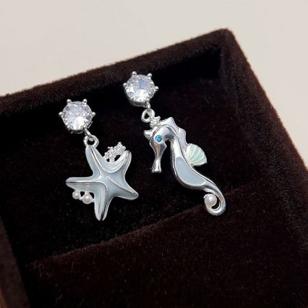 Vista dettagliata degli orecchini in argento a tema marino, evidenziando la stella marina con perle e il cavalluccio marino con una pietra blu.