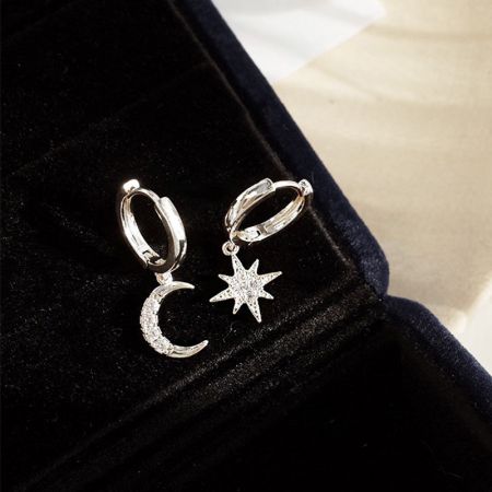 Primo piano degli orecchini huggie a forma di stella e luna in argento sterling 925, che mostrano i dettagli intricati delle pietre.