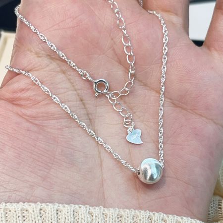 Vista del cierre del collar y la cadena de extensión, con un pequeño detalle de charm en forma de corazón.