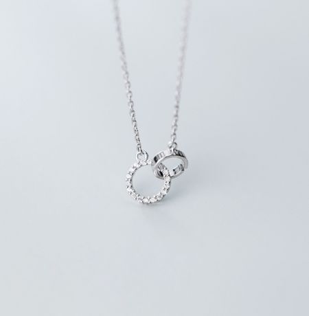 Collar de Círculos Entretejidos en Plata de Ley 925 - Un primer plano del collar de círculos entrelazados en plata de ley 925, mostrando la detallada artesanía de los dos anillos entrelazados, uno de los cuales está elegantemente pavimentado con brillantes piedras de circonita.