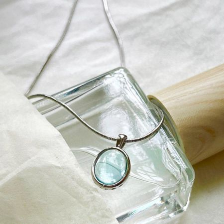 A close-up of a silver necklace with a light blue gemstone pendant.