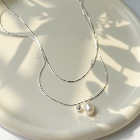 Collar de perlas con cadena de plata esterlina 925 - Un primer plano del collar de perlas con cadena de plata esterlina 925, que muestra la fina cadena, la perla de agua dulce redonda y el pequeño colgante de bola de plata contra un fondo blanco.