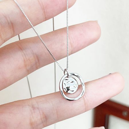 Collier en argent sterling 925 en gros avec cercle évidé et charme en disque martelé. - Gros plan d'un collier en argent sterling 925 présentant un cercle évidé et un charme en disque martelé, sur fond blanc.