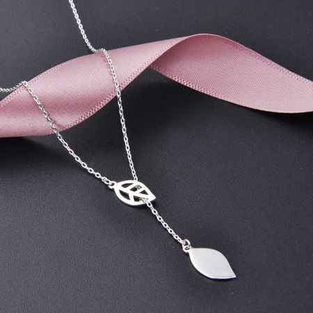 Collar de hoja de plata presentado con estilo contra un fondo oscuro con una cinta decorativa rosa.