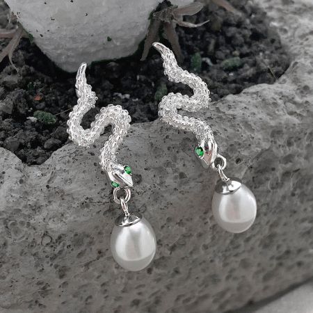 Zijaanzicht van de zilveren slang parel drop oorbellen met groene edelsteen ogen.