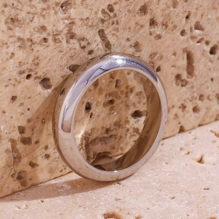 The simple and elegant silver stainless steel band ring resting on a textured stone surface.