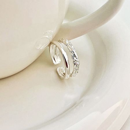 Een enkele sterling zilveren ring met een unieke textuur die op de rand van een theekop rust, wat het delicate ontwerp benadrukt.