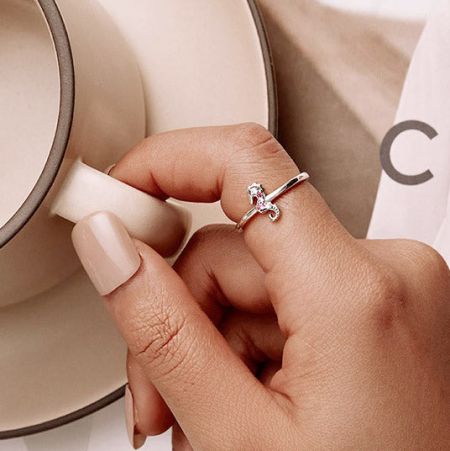 An elegant silver ring with a sparkling diamond, shown on a hand holding a teacup.