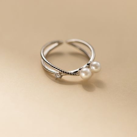 Ensemble de 5 bagues ajustables en argent sterling 925 avec perles en croisement. - Gros plan d'une bague ajustable en argent sterling 925 avec perles, issue du set de 5 pièces, présentant un design de bande torsadée avec une pierre en zirconium cubique et deux perles.