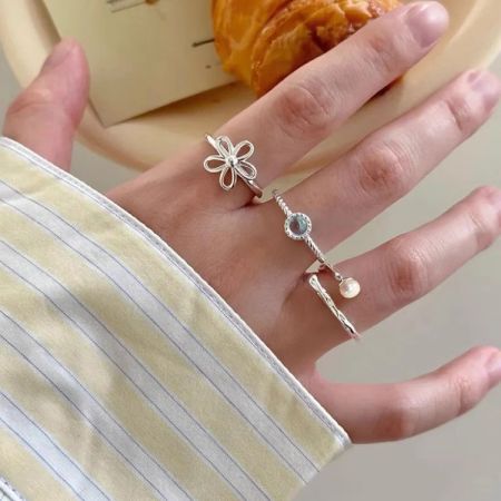 Due anelli in argento sterling del set regolabile, uno con un design floreale e l'altro con un motivo di spilla di sicurezza, indossati sulla mano di un modello per mostrare scala e stile.