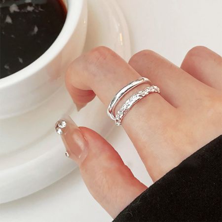 Een hand van een model die de dual-laags twee-textuur zilveren ringen draagt terwijl ze een koffiekop vasthoudt, wat hun stijlvolle aantrekkingskracht toont.