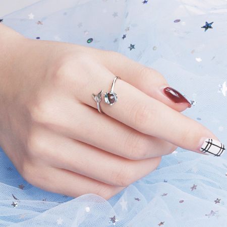Die Hand des Modells trägt mehrere Ringe aus Sterlingsilber aus der Meerjungfrauen-Schwanz-Kollektion vor einem sanften blauen Hintergrund.