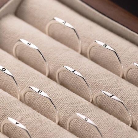 A collection of 925 sterling silver letter rings elegantly arranged in a beige jewelry box.
