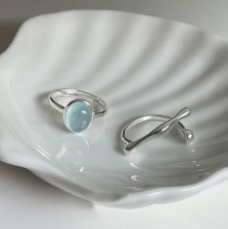 Bague en argent sterling 925 avec cristal bleu - Une bague en argent sterling 925 avec une pierre en cristal bleu clair, présentée élégamment sur un plat en céramique blanche.