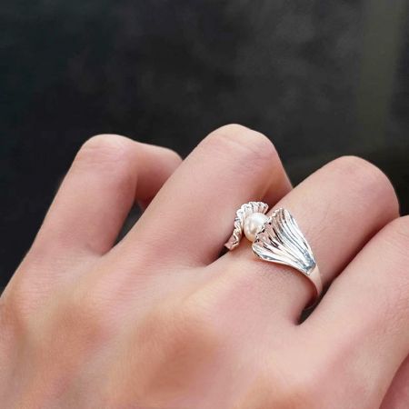 Bagues ajustables en perles de coquillage de style français en argent sterling 925. - Une bague ajustable en argent sterling 925 présentant un élégant design de coquille Saint-Jacques de style français tenant une seule perle lustrée, portée sur un doigt.