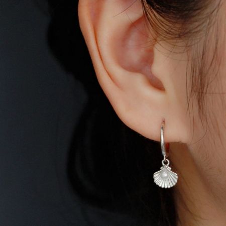 Modello che indossa l'orecchino a cerchio huggie in argento sterling 925 con perla oceanica.