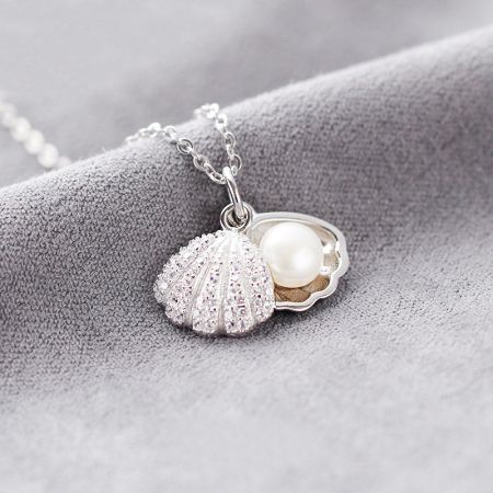 Collar con colgante de perla en concha de mar de plata esterlina 925 - Primer plano de un colgante de concha de mar de plata esterlina 925, revelando una delicada perla anidada en su interior. El colgante tiene un acabado pulido y brillante.
