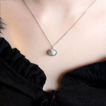 Una toma clara en estudio del colgante del collar en forma de concha de plata contra un fondo blanco.
