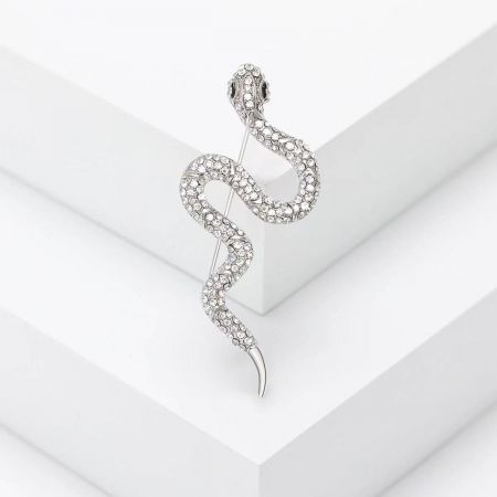 Broche de serpiente de strass creativo – Pin de animal minimalista y a la moda - Un primer plano del broche en forma de serpiente plateada, intrincadamente incrustado con brillantes piedras preciosas claras, exhibido sobre una superficie blanca.
