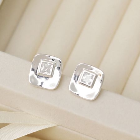 Pendientes de perno cuadrados de CZ plateados en plata presentados elegantemente en una caja de joyería de color crema.