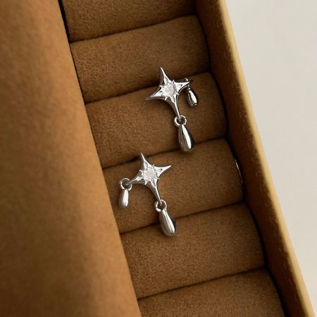 Primer plano de los pendientes Star Drop presentados en una lujosa caja de joyería de terciopelo marrón, mostrando el diseño de estrella de plata y el charm en forma de lágrima.