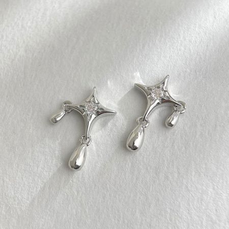 Un par de pendientes en forma de estrella de plata con piedras de zirconia CZ claras y brillantes y elegantes charms en forma de lágrima sobre un fondo blanco.