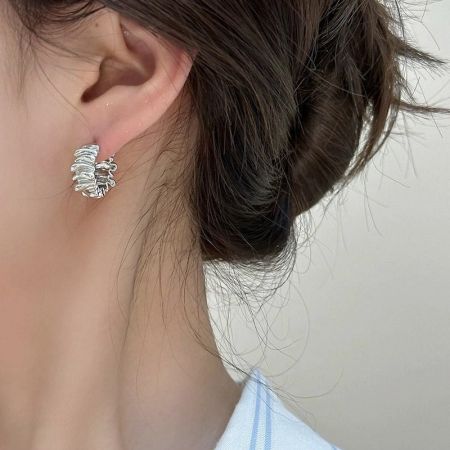 Primo piano di una donna che indossa orecchini a cerchio in argento 925 con pieghe irregolari a forma di C, mostrando la loro vestibilità e stile.