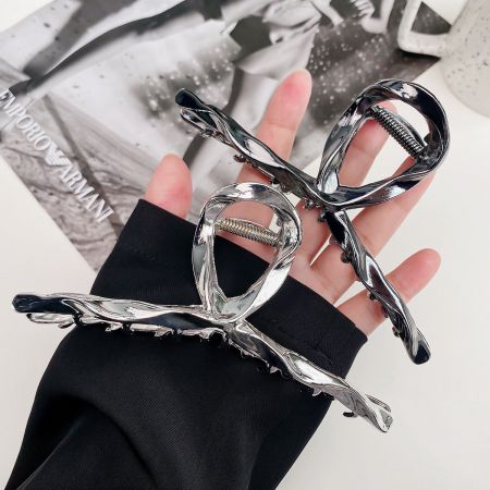 A hand holding two silver hair clips, highlighting their unique twisted design and metallic sheen.