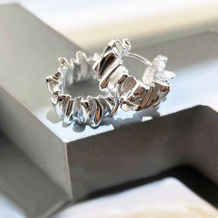 Gli orecchini a cerchio in argento 925 con pieghe sono presentati elegantemente su una scatola di gioielli bianca.
