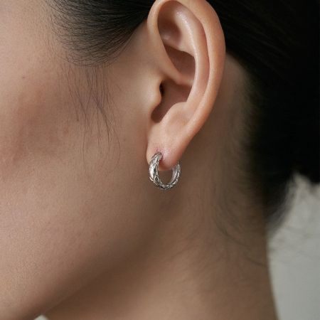 Primo piano dettagliato dell'orecchino a cerchio trapuntato in argento sterling sull'orecchio di un modello.