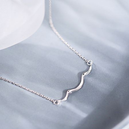 Vista detallada del collar con colgante de ola de plata.