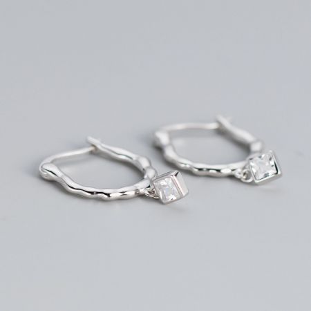 Profil latéral des boucles d'oreilles en argent ondulées mettant en valeur la texture et la pierre précieuse transparente.