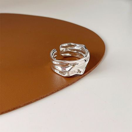 Toma de cerca del anillo abierto de plata con pliegues irregulares, mostrando su diseño ondulado único.