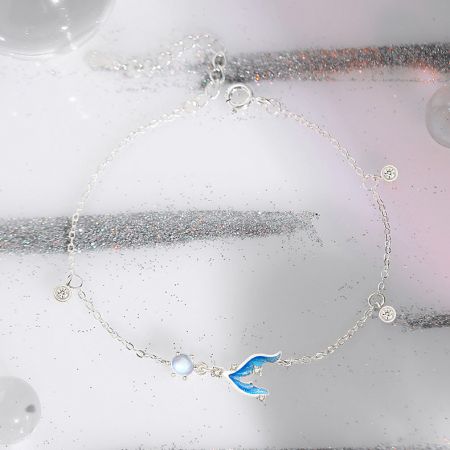 Gros plan sur un bracelet en argent avec un charme en émail bleu et blanc en forme de baleine.