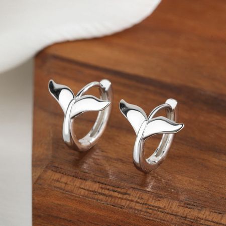 Un paio di orecchini a forma di coda di sirena in argento sterling 925 su uno sfondo di legno.