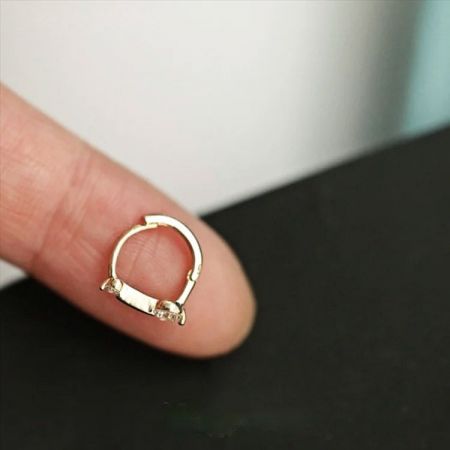 La dimensione delicata di un piccolo orecchino huggie in zirconia è mostrata su una punta di dito per scala.