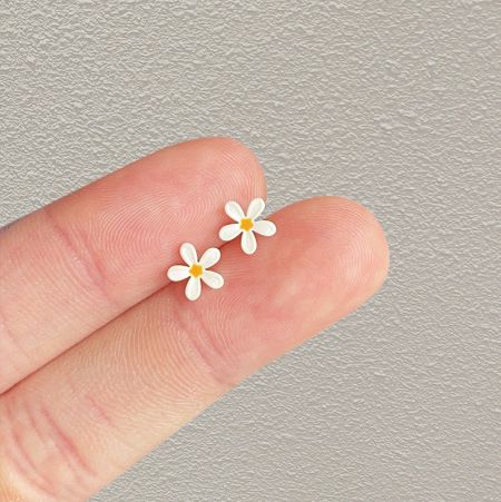 Los pequeños pendientes de flor de margarita blanca sostenidos entre los dedos para mostrar su escala en miniatura.