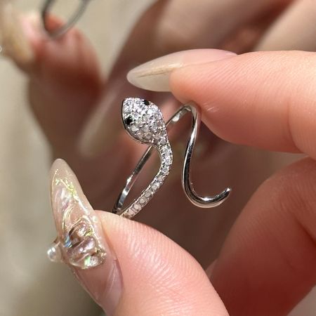 Set di 5 anelli a forma di serpente in argento S925 con zirconia cubica - Un primo piano dettagliato di un anello a forma di serpente in argento sterling 925, adornato con scintillanti pietre di zirconia cubica trasparente, tenuto tra due dita.