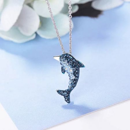 Un collar de colgante de delfín de plata brillante, decorado intrincadamente con piedras azules y claras que brillan.