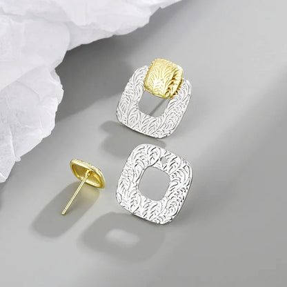 Primo piano della finitura in argento testurizzato e degli accenti in oro sugli orecchini quadrati geometrici cavi.