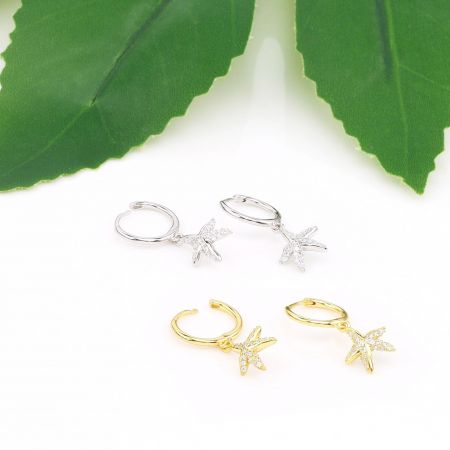 Due paia di orecchini huggie a forma di stella marina, uno in argento e uno in oro, presentati affiancati.