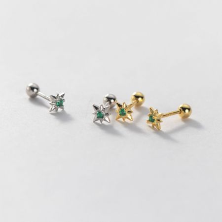 Close-up of silver and gold star earrings with vibrant green gemstones.