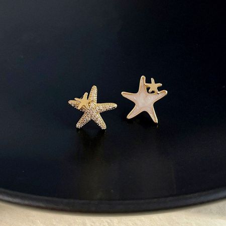 Brincos assimétricos de estrela do mar com zircônia e designs em ouro liso sobre um fundo preto.