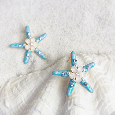 樹脂の花と真珠のスタッドピアスの手作りヒトデ(5ペア) - 中央に真珠と樹脂の花をあしらった青と白の詳細を持つ手作りのエナメルヒトデスタッドピアスのペアで、ビーチをテーマにしたデザインを展示。