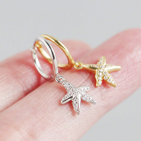 Dettaglio ravvicinato degli orecchini a forma di stella marina in oro e argento, evidenziando le decorazioni in pietra trasparente.
