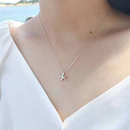 Close-up of the silver starfish necklace worn by a model in a white blouse.
