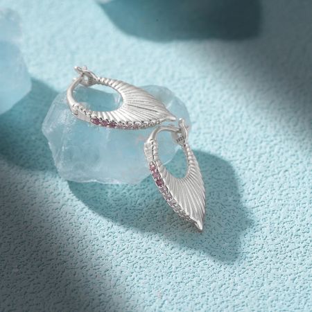 Scatto dettagliato degli unici orecchini a coda di sirena in argento sterling, con un motivo a squame testurizzato e gemme rosa.