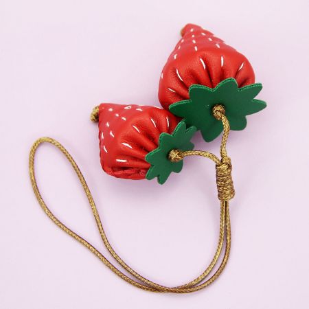 Two strawberry-shaped charms with green leaves and a durable gold cord for easy attachment.